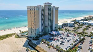 A high-rise hotel with a pool and beach access, surrounded by a parking lot and ocean views.
