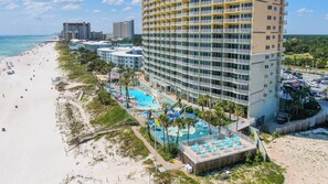 Un hotel frente a la playa con varias piscinas, una playa y un horizonte urbano de fondo.