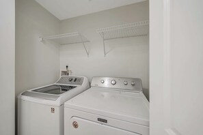 A laundry room with two white washing machines and two drying racks.