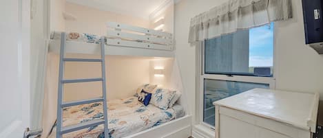 A bunk bed with a ladder, a window with curtains, a small cabinet, and a wall-mounted TV.
