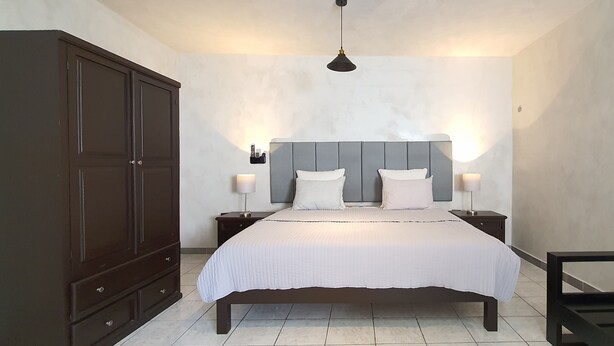 A bedroom with a large bed, two bedside tables with lamps, a wardrobe, and a hanging light fixture. - Cozumel 568 - Vacation Rental (Cozumel)