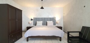 Une chambre à coucher avec un grand lit, deux tables de chevet avec des lampes, une armoire et un luminaire suspendu.