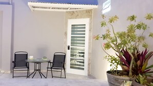 A small patio area with two chairs and a table, a potted plant, and a door with frosted glass panels. - Cozumel 568 - Vacation Rental (Cozumel)