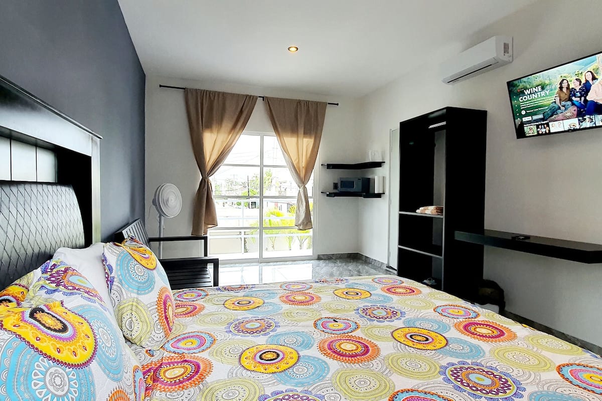 A modern hotel room with a large bed, a TV mounted on the wall, and a window with curtains.