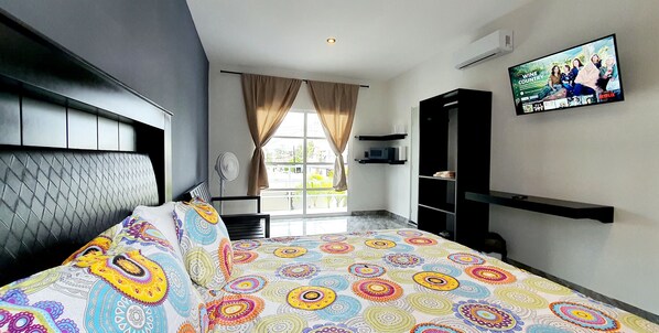Une chambre d’hôtel moderne avec un grand lit, un téléviseur fixé au mur et une fenêtre avec des rideaux.