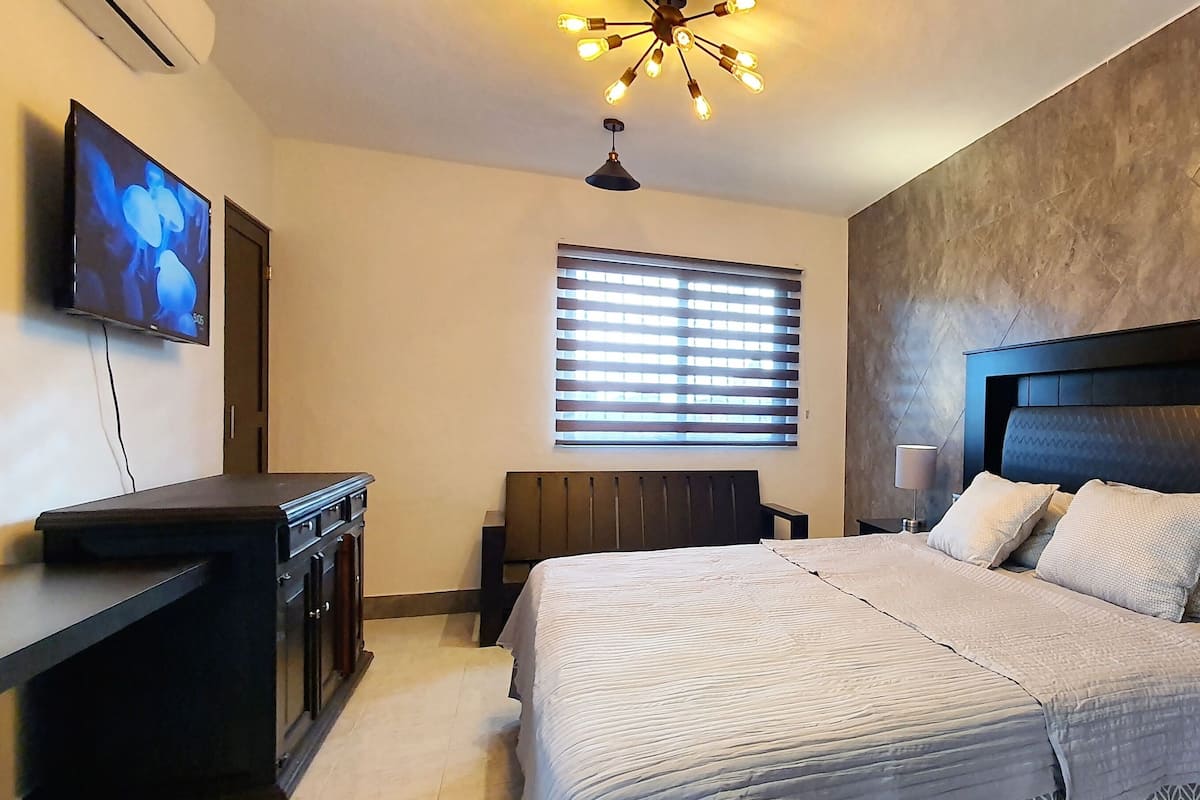 A modern bedroom with a large bed, a TV mounted on the wall, and a ceiling light fixture.