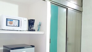 A kitchenette with a microwave, coffee maker, and utensils on a shelf, a refrigerator, and a sliding glass door closet. - Cozumel 568 - Vacation Rental (Cozumel)