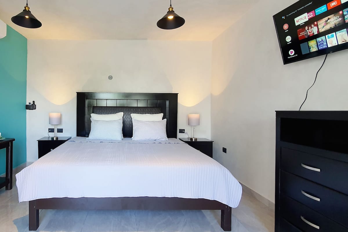 A modern hotel room with a large bed, bedside lamps, a TV mounted on the wall, and a small table with cups.