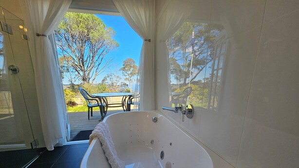 A modern bathroom with a freestanding bathtub, a glass shower enclosure, and a view of an outdoor deck with a table and chairs. - MOUNTAIN VIEWS fireplace SPA 5 bedrooms, air-cond, early checkin & late checkout (Wentworth Falls)