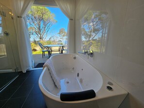 Ein modernes Badezimmer mit freistehender Badewanne, einer Duschkabine aus Glas und Blick auf eine Terrasse mit Tisch und Stühlen.