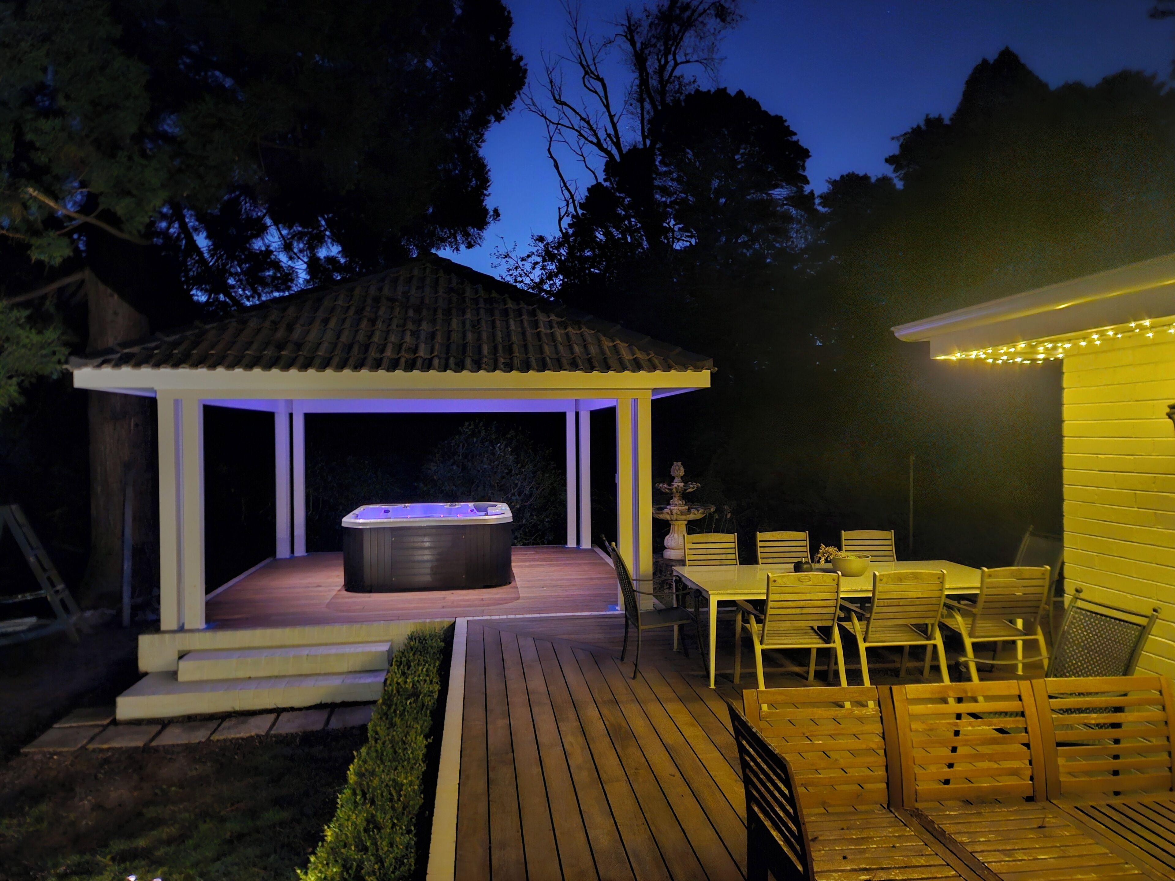 A gazebo with a hot tub, outdoor seating, and string lights.