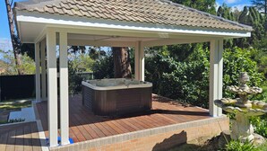A covered outdoor hot tub area with a pergola roof, surrounded by a brick patio and a garden with a fountain. - MOUNTAIN VIEWS fireplace SPA 5 bedrooms, air-cond, early checkin & late checkout (Wentworth Falls)