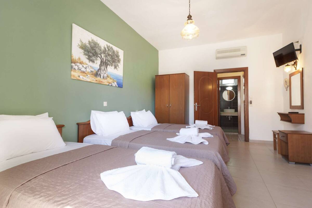Ein Hotelzimmer mit zwei Betten, einem Baumgemälde, einem Schrank, einem Badezimmer mit Spiegel und einem Fernseher.
