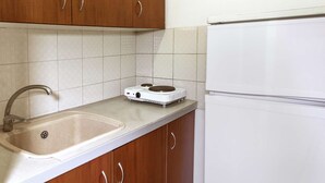 A kitchen with wooden cabinets, a sink, a stove, and a white refrigerator. - galini.apartments (Kassandra)