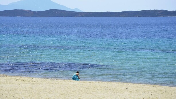 A beach with a person in a blue dress, clear water, and distant mountains. - galini.apartments (Kassandra)