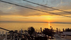 A beachside view with umbrellas and lounge chairs, a sunset, and a calm sea. - galini.apartments (Kassandra)