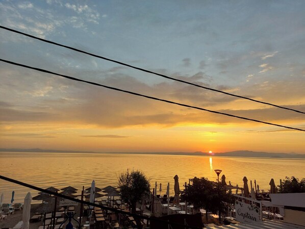 A beachside view with umbrellas and lounge chairs, a sunset, and a calm sea.