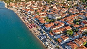 An aerial view of a coastal town with tightly packed buildings, a beach with umbrellas, and a clear view of the sea. - galini.apartments (Kassandra)