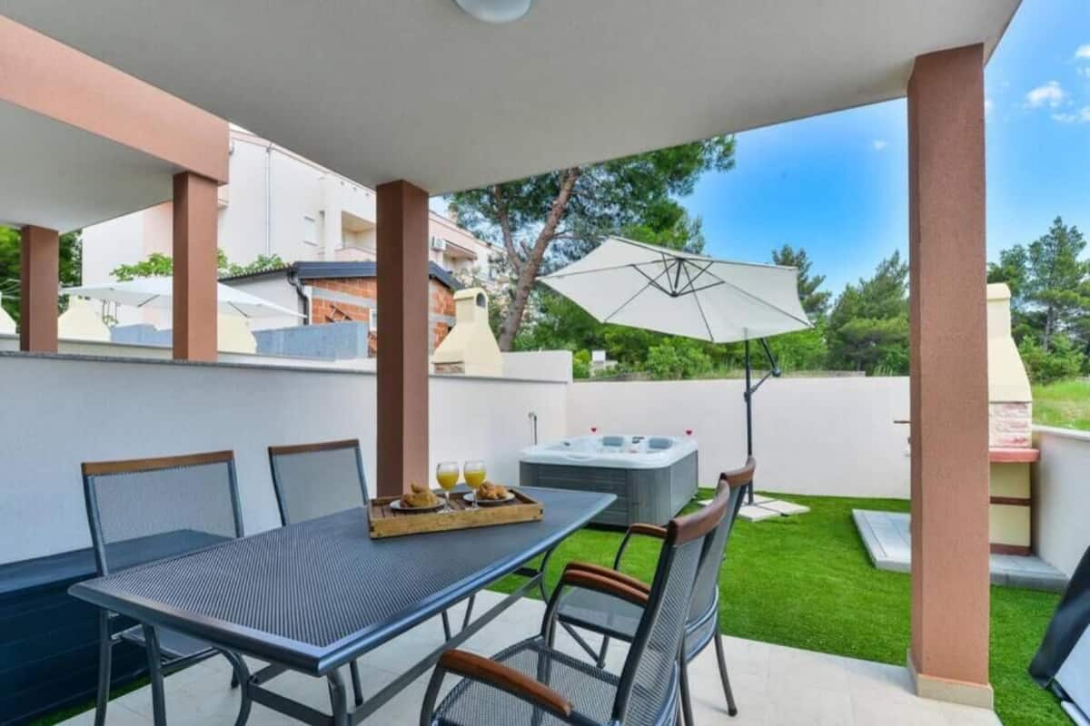 An outdoor patio with a table set for two, a hot tub, and a large umbrella.