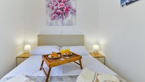 A neatly made bed with a wooden tray holding breakfast items, two bedside lamps, and a floral painting on the wall. - Cascade villas with private garden and jacuzzi (Starigrad)