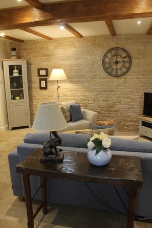 Un salon avec un mur en pierre, un canapé, une lampe, un téléviseur et un meuble.