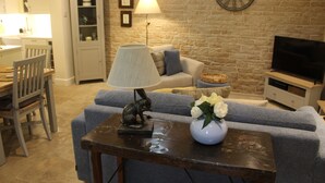 Een woonkamer met een bank, een tafel met een lamp en bloemen, een televisie en een bakstenen muur.