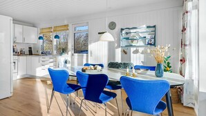 Una cocina moderna con armarios blancos, una mesa de comedor con sillas azules y un amplio ventanal que proporciona luz natural.