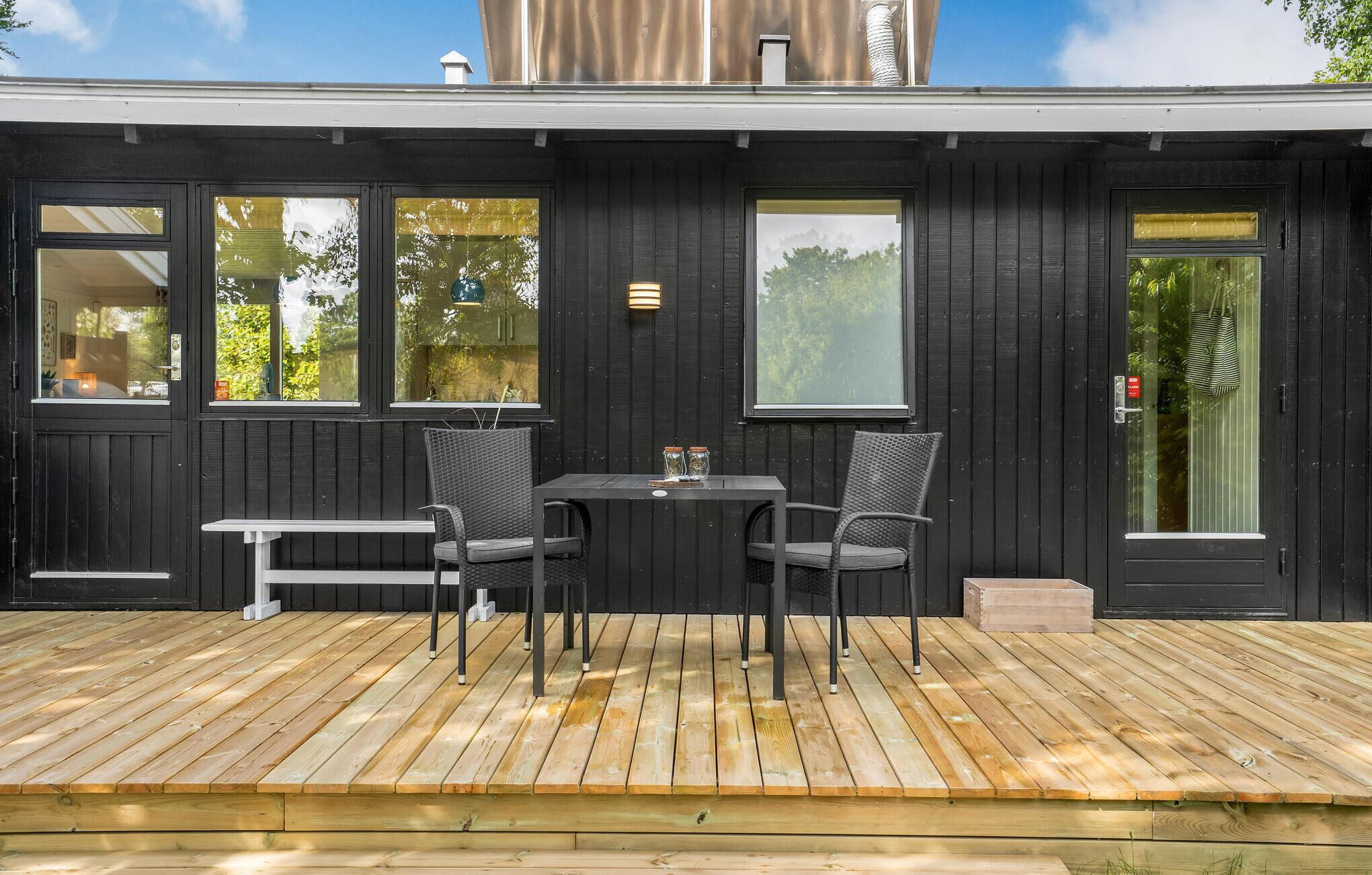 A modern outdoor seating area with a wooden deck, two tables, and four chairs.