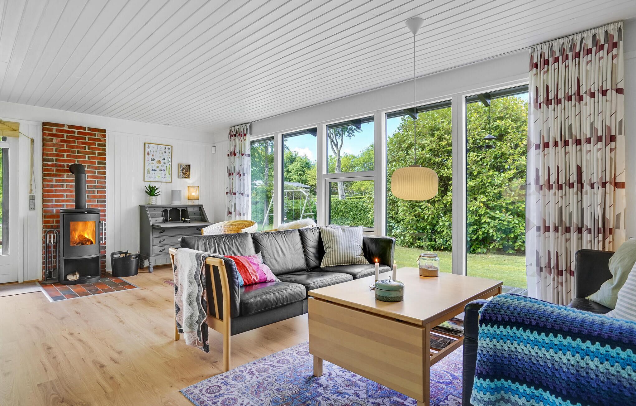 Ein gemütliches Wohnzimmer mit Kamin, einer Couch, einem Esstisch und großen Fenstern mit Blick auf den Garten.