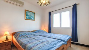 A bedroom with a wooden bed, a nightstand with a lamp, a window with curtains, and a painting on the wall. - 2 bedroom stunning home in Roquebrune-sur-Argens (Roquebrune-sur-Argens)