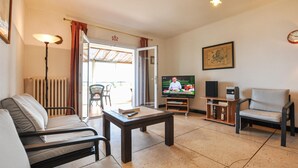 A living room with a sofa, armchair, TV, and a table. There's a door leading to an outdoor area with chairs. - 2 bedroom stunning home in Roquebrune-sur-Argens (Roquebrune-sur-Argens)