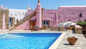 Un área de piscina con un muro de piedra, un edificio rosa y una escalera.