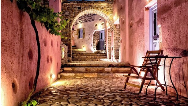 Un patio empedrado con una silla y una mesa de madera, que conduce a un arco de piedra y una puerta.