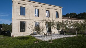 A two-story building with a symmetrical facade, large windows, and a gravel courtyard with outdoor seating.