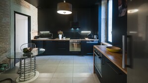 A modern kitchen with a central island, black cabinetry, stainless steel appliances, and a hanging light fixture.