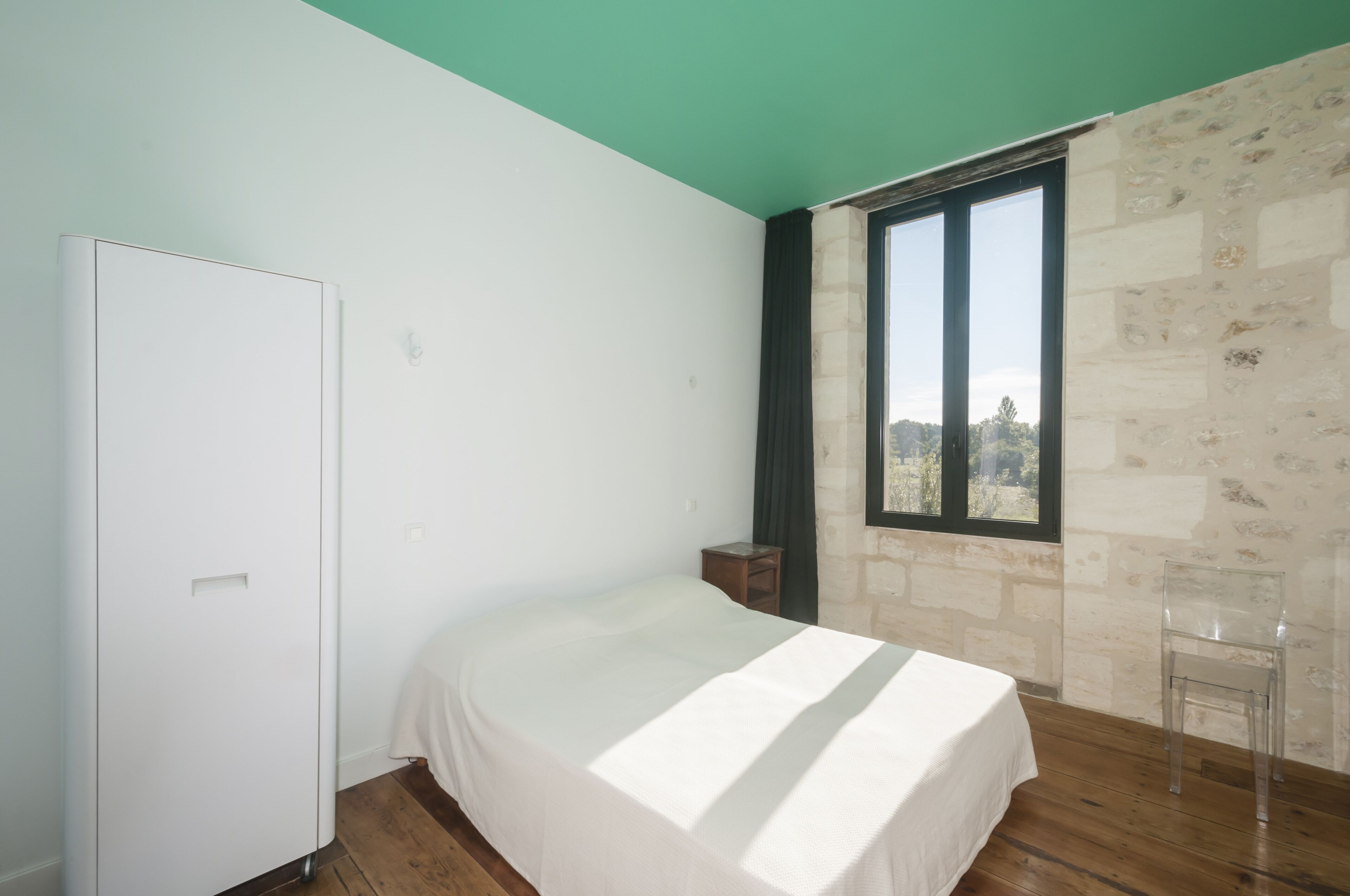 A bedroom with a bed, a wardrobe, a window with a view, and a stone wall.