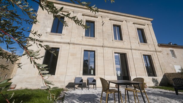 A two-story building with a symmetrical facade, large windows, and a gravel patio with outdoor seating.