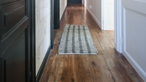 A hallway with wooden flooring, a patterned rug, and a door on the left.
