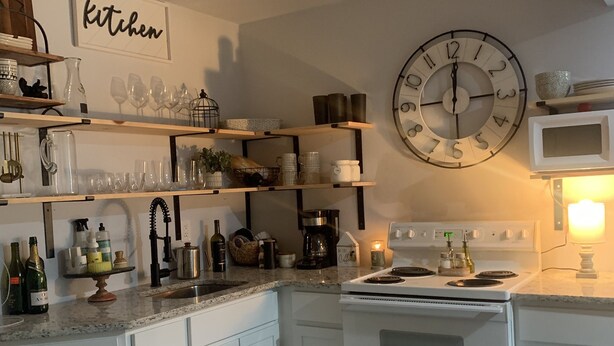 Una cocina moderna con armarios blancos, un reloj de pared grande y una variedad de utensilios de cocina en estantes.