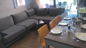 Ein modernes Wohnzimmer mit einem grauen Sofa, einem Esstisch gedeckt mit Tellern und Gläsern, und Blick auf die Stadt durch große Fenster.