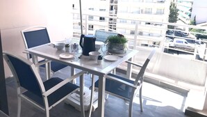 Ein Balkon mit Tisch für zwei Personen, Stühlen, einer Kaffeekanne und einer kleinen Pflanze.