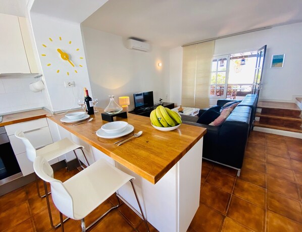 A modern kitchen with a wooden countertop, white chairs, and a dining table set for two.
