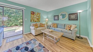 A living room with two sofas, a coffee table, and a floor lamp. There is a large window and a door leading outside. - Summer Retreat - Prime Location | Sleeps 8 | Pets (Destin)