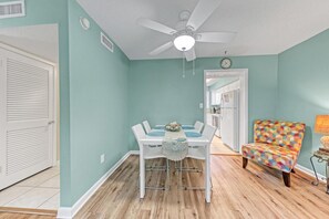 A dining area with a white table and chairs, a ceiling fan, and a colorful armchair. - Destin Getaway | Private Beach | Pools | Pets OK (Destin)