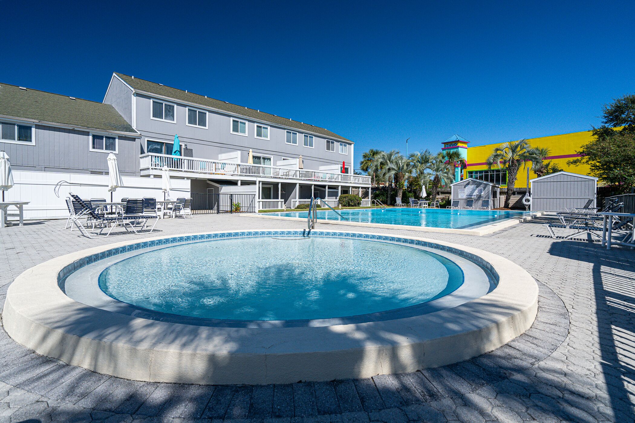 Une piscine de forme circulaire, entourée de chaises longues et d’un bâtiment doté d’un balcon.