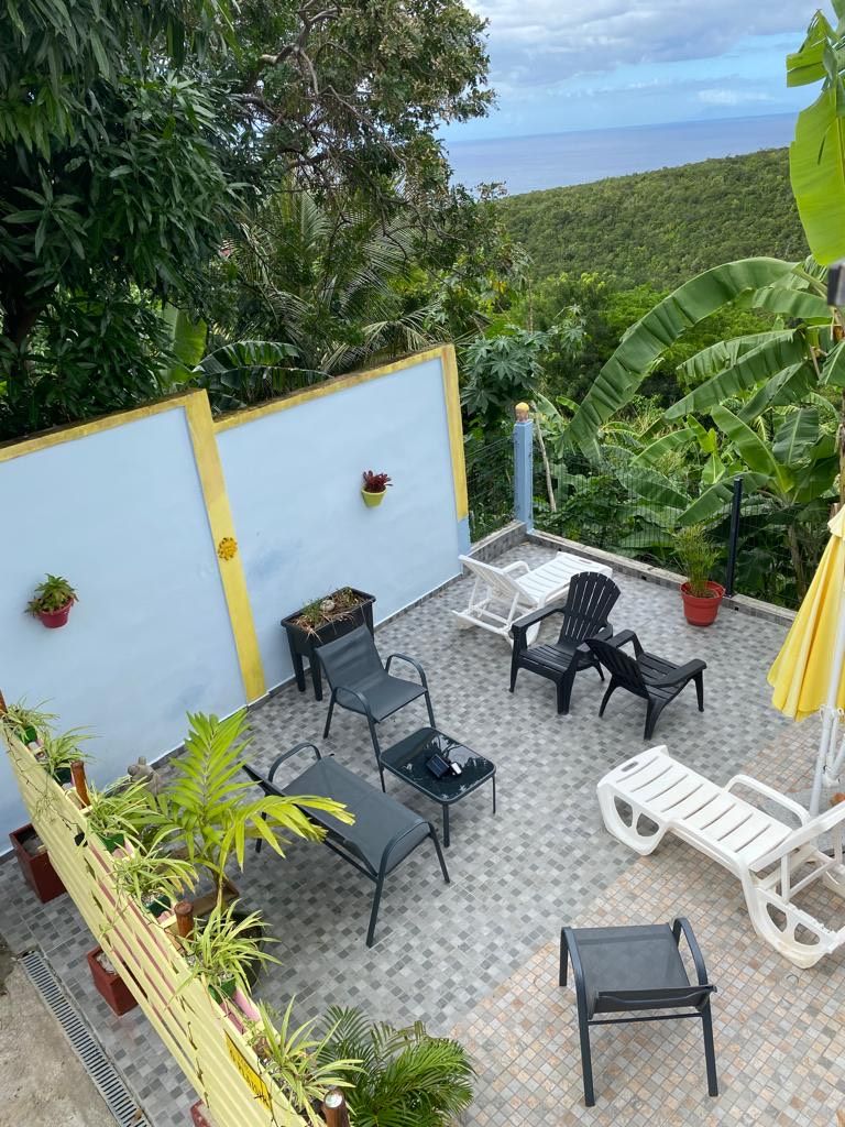 A rooftop patio with outdoor furniture, potted plants, and a view of the ocean.