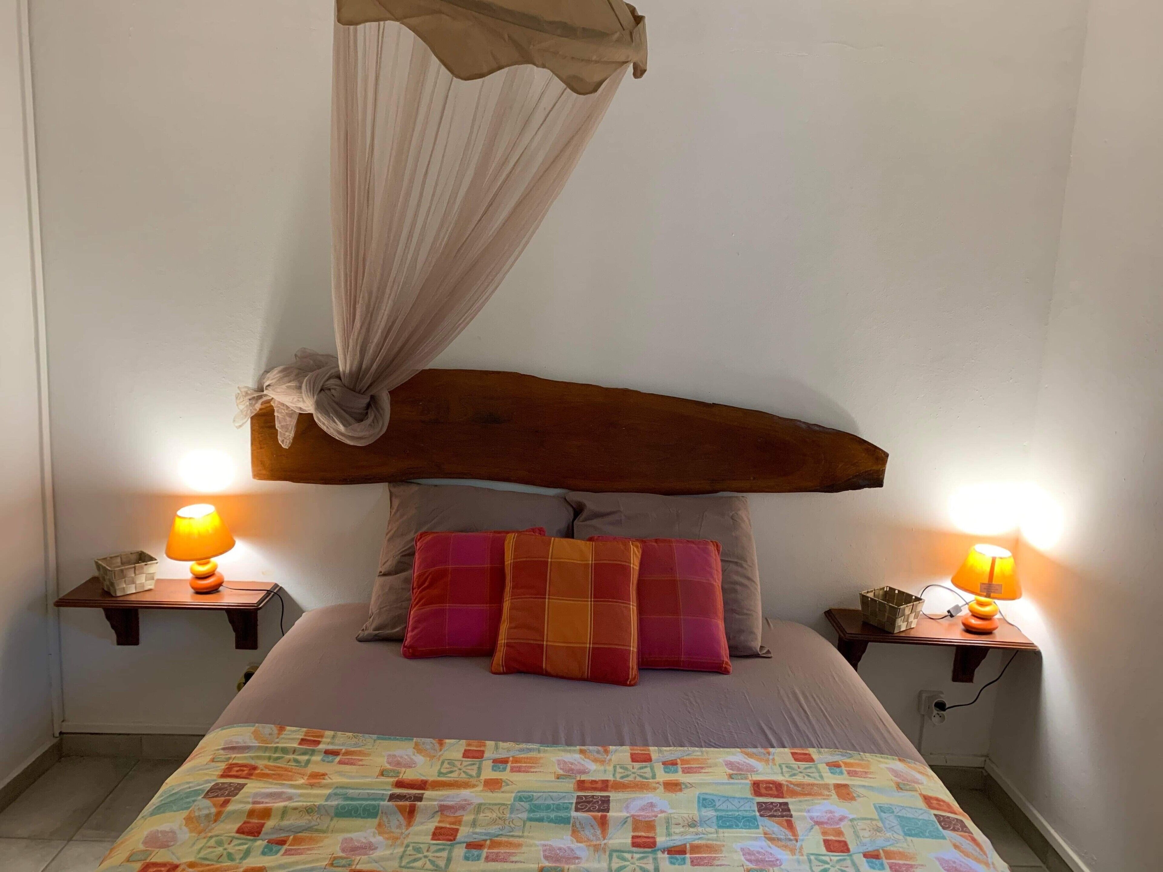 A bedroom with a wooden headboard, a canopy, two bedside tables with lamps, and a colorful quilt.