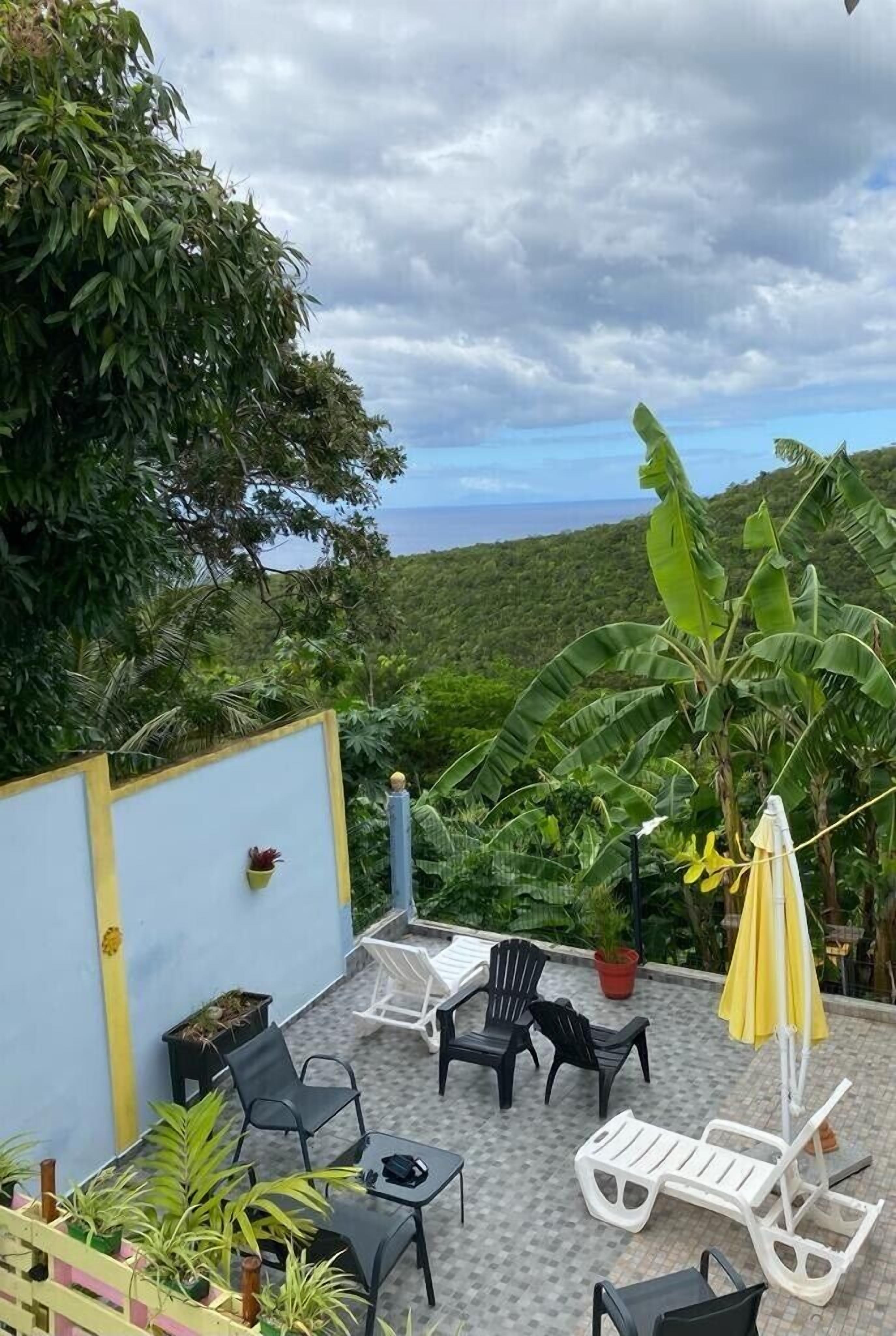 A patio with outdoor furniture, a yellow umbrella, and a view of a lush landscape.