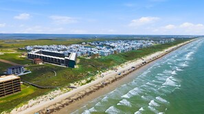 An aerial view of a coastal residential area with a beachfront, a large building complex, and a long stretch of beach.