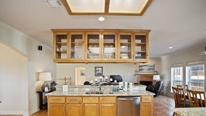 A kitchen with a central island, wooden cabinets, a dishwasher, and a dining area with chairs. - Casa de la Perla, Ocean Views & Beach Boardwalk (Port Aransas)